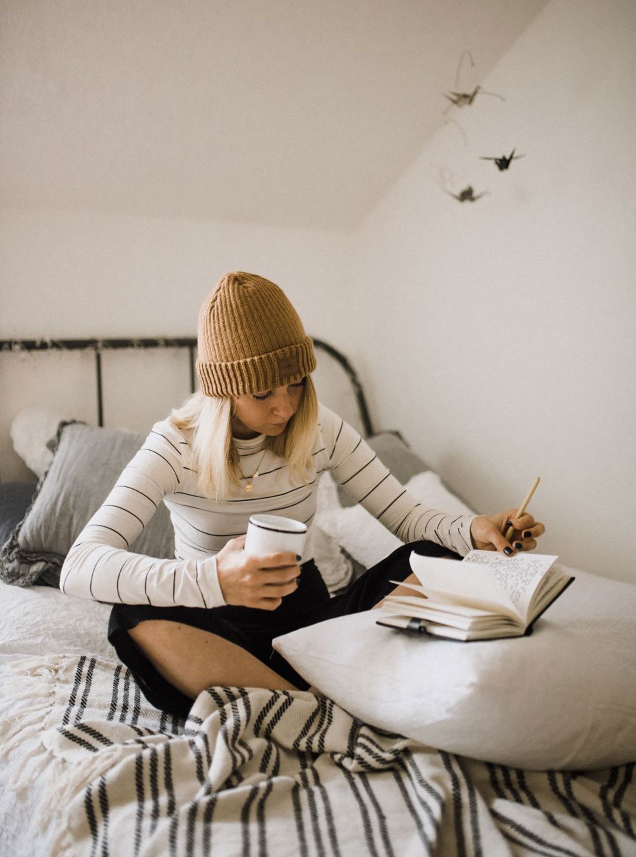 Ei jente sit oppi ei seng med ein kaffikopp i handa og skriv