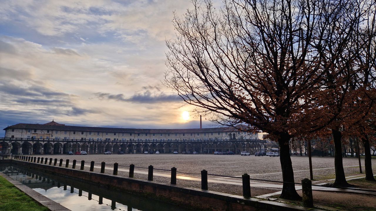 Open plass med ein gamal bygning i bakgrunn med solnedgang og eit tre i framgrunn
