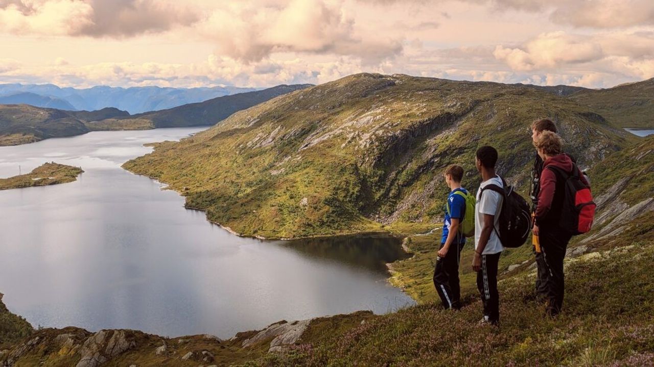 Fire gutar står på ein fjelltopp og ser utover eit fjellvatn