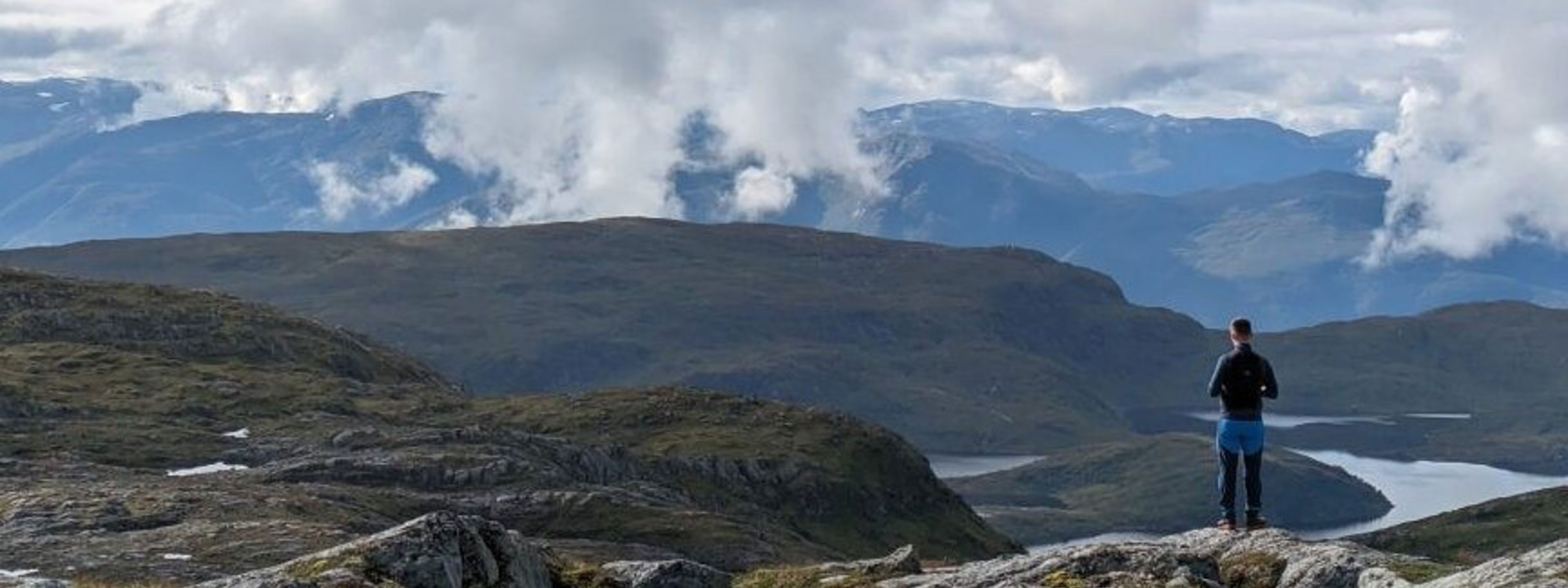 Ein elev står på ein fjelltopp og ser utover
