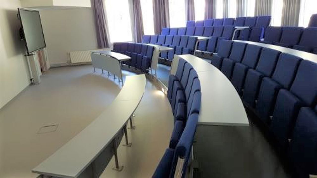 Eit auditorium beståande av fleire stolar etter kvarandre med bord framfør.