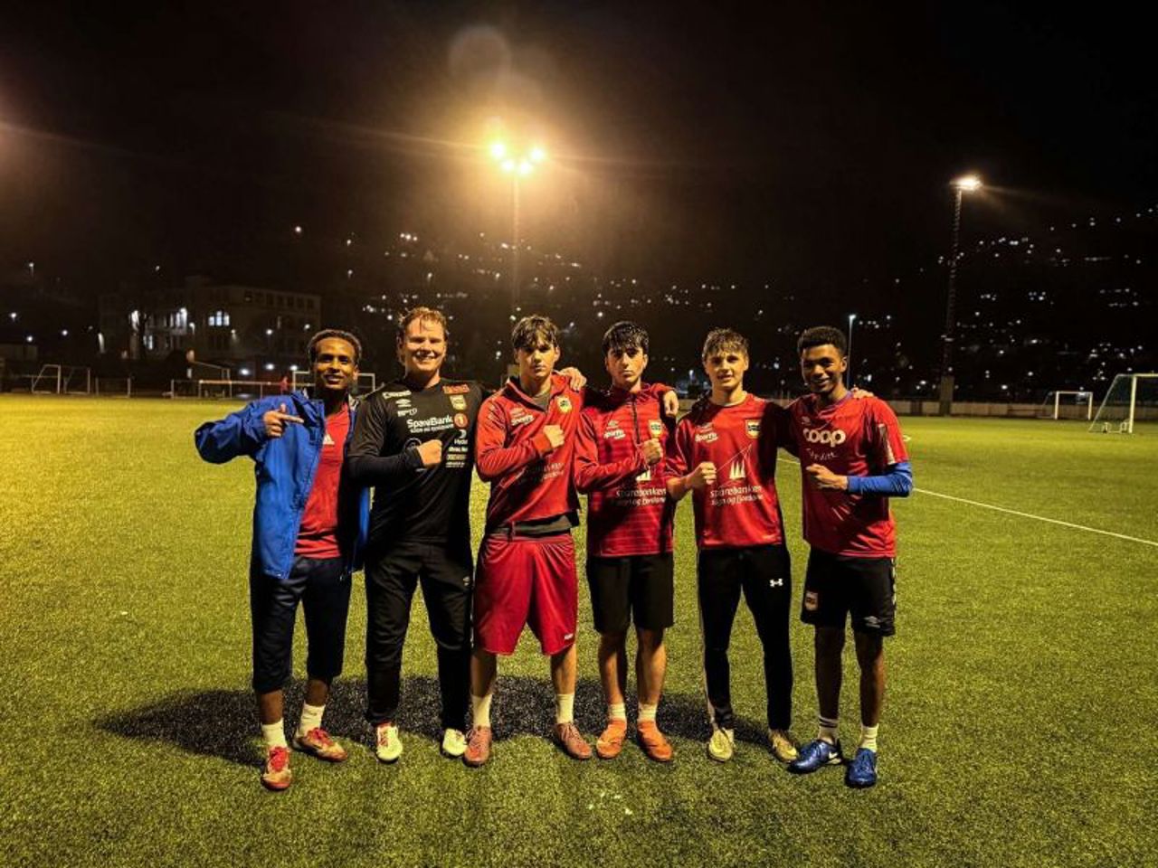 Seks gutar står på rekke under trening på ei kunstgrasbane