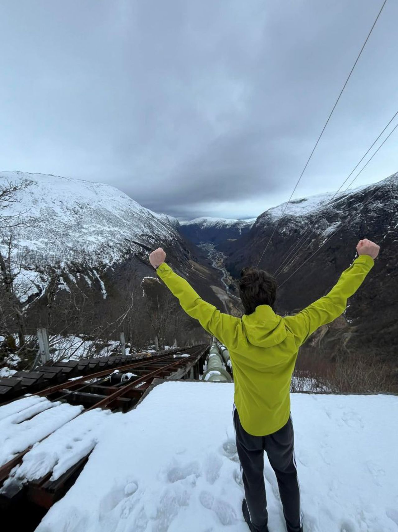 Ein gut står med armane i været øverst oppe i ei trapp og ser utover mot fjella
